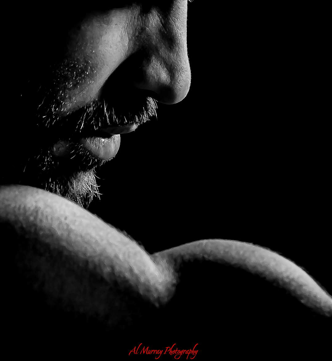 Dramatic black and white close up portrait showing the lower half of a man’s face and shoulder against a dark background. Strong side lighting highlights the texture of his beard, lips, and skin in the bold style of a specialized portrait photographer in Southwestern Ontario.