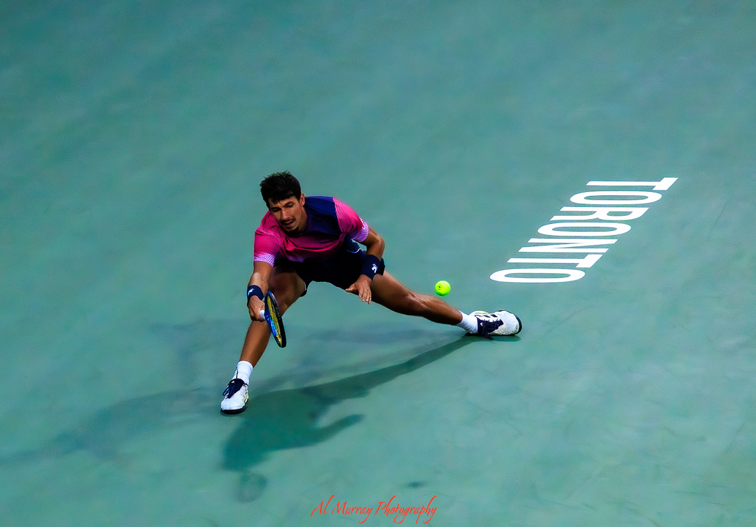 Tennis player lunges low across the court to return a fast shot during a match in Toronto. The wide angle composition and dramatic movement highlight the skill and timing captured by a tennis photographer in Canada.